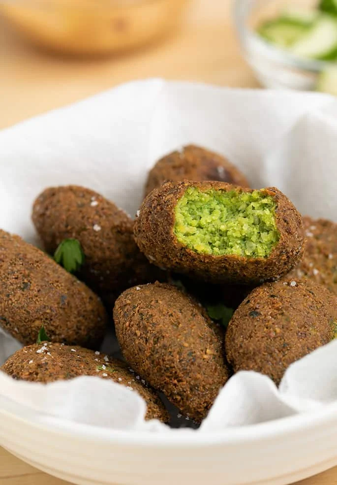 Pile of falafel in white bowl one with bite taken