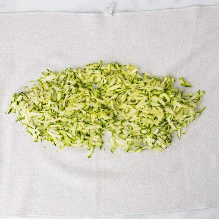pile of light and dark green fresh zucchini shreds on open white towel