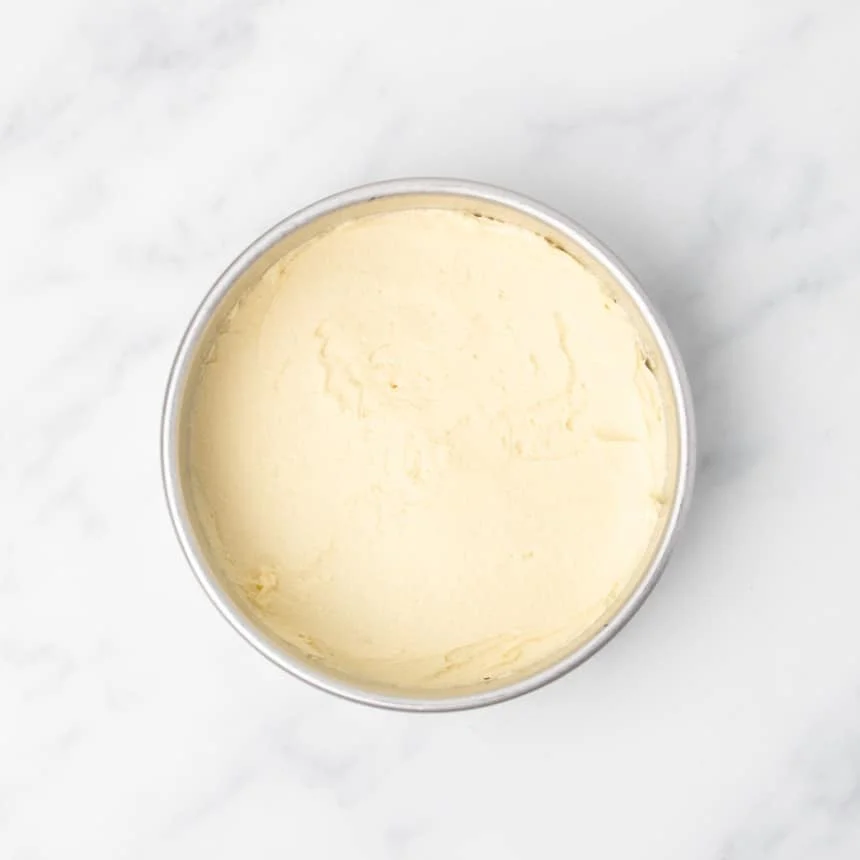 Plain yellow raw cake batter spread evenly on bottom of a round metal cake pan.