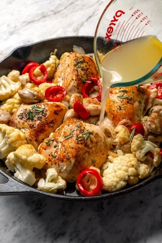 Pouring broth into pan of chicken scarpariello.