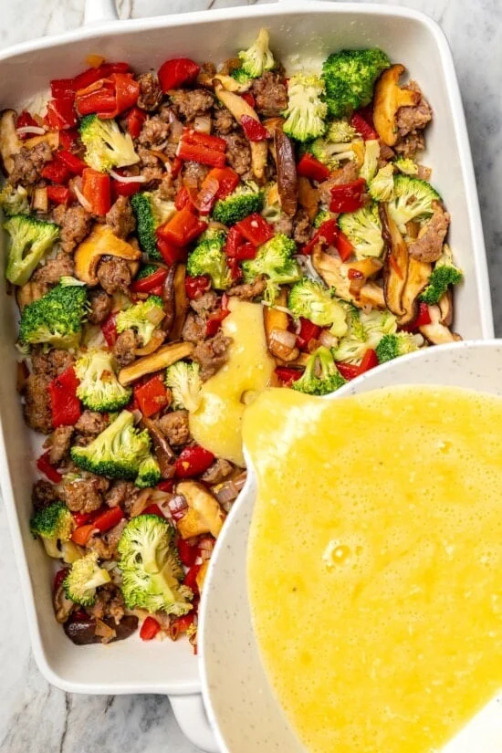 Pouring egg over vegetables and sausage for breakfast casserole.