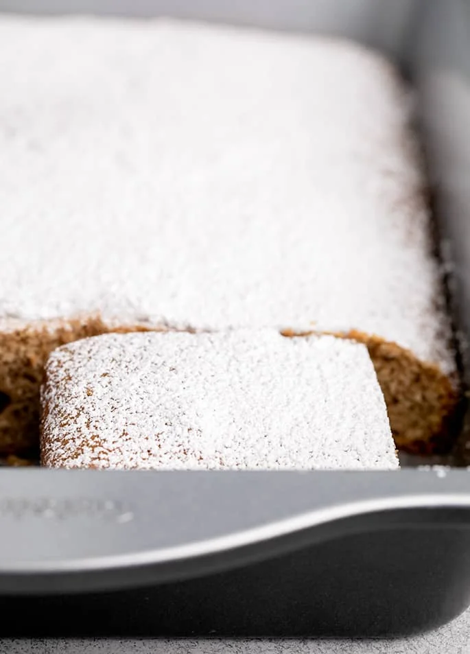 Powdered sugar on light brown spice cake in pan with a couple pieces missing