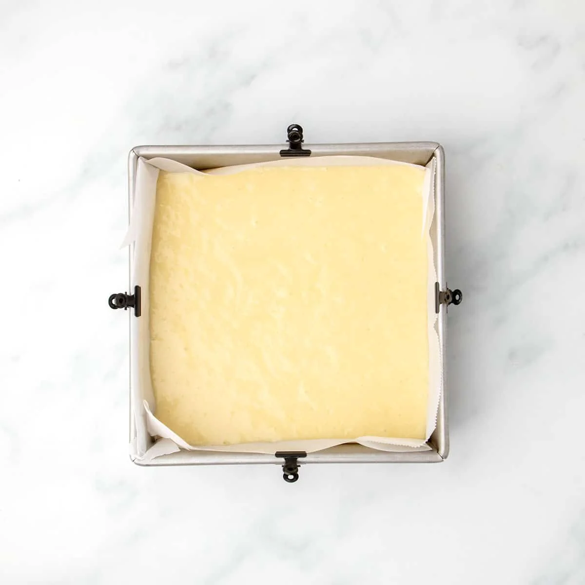 Prepared cake batter evenly spread in a parchment-lined square baking pan, ready for the oven.