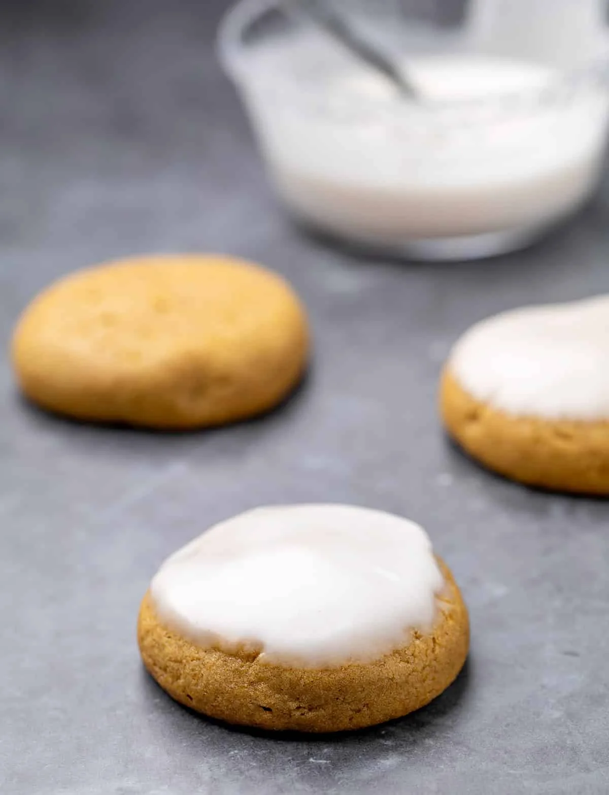 Pumpkin cookies with icing and without with bowl of icing in background.