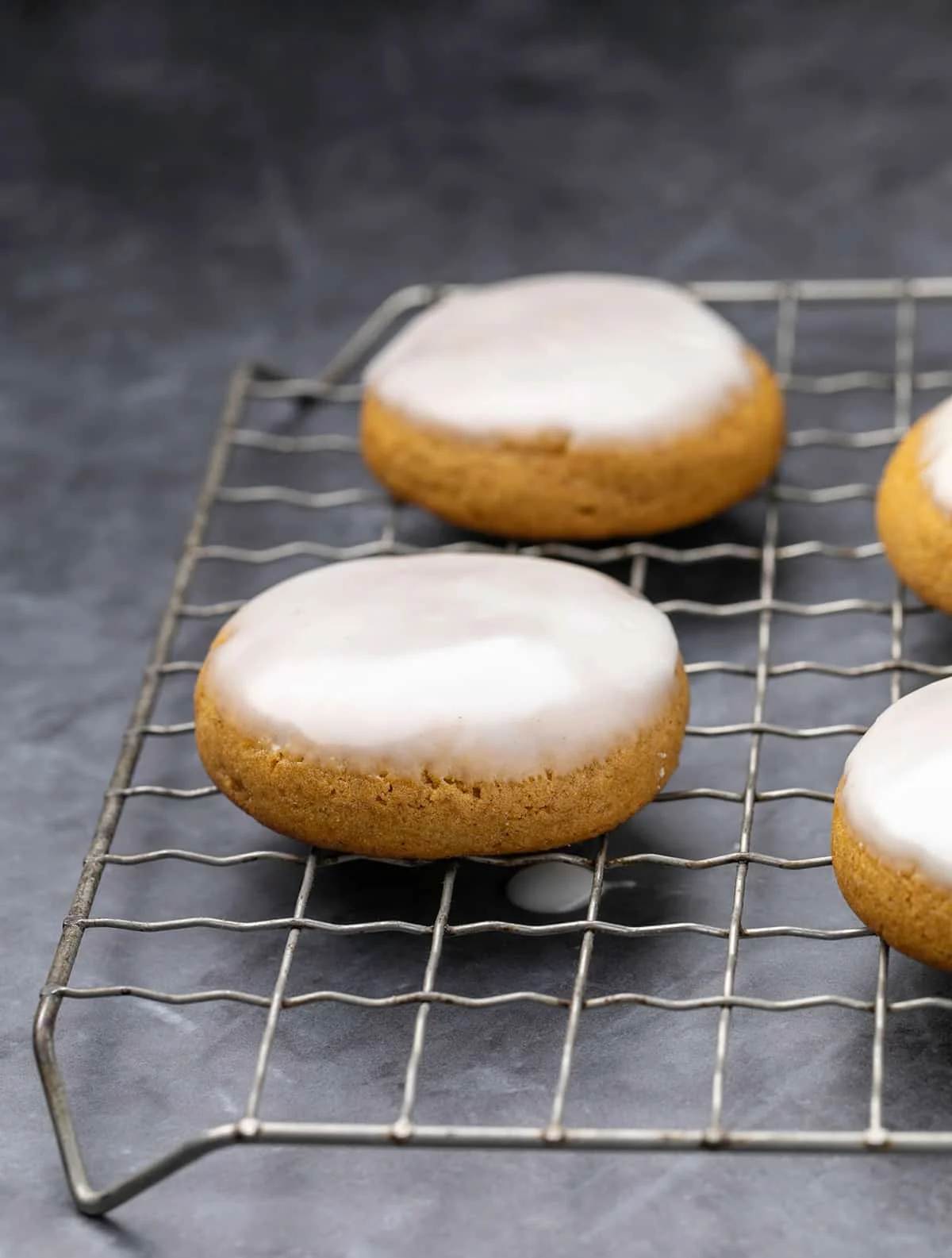 Pumpkin cookies with white icing dripping on wire rack.