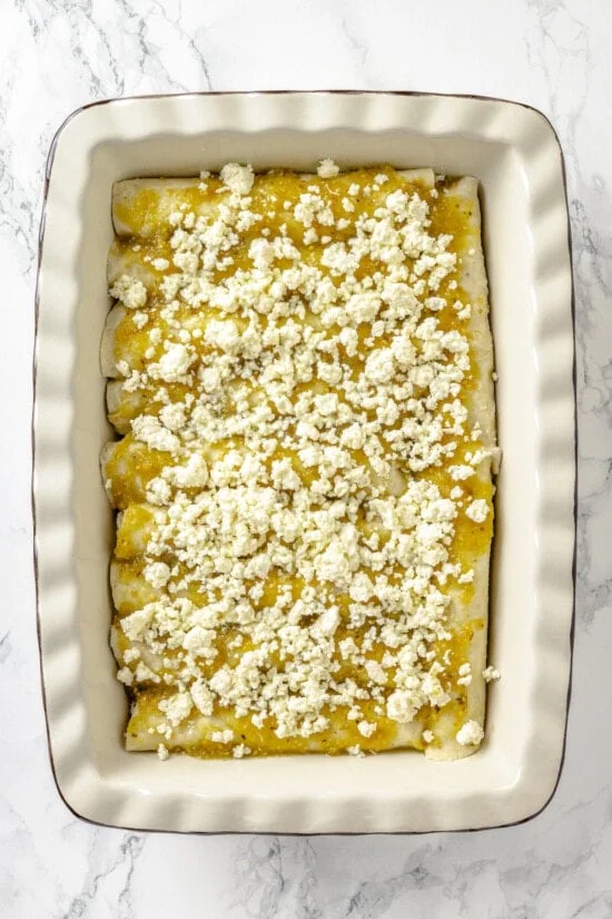 Queso fresco on top of salsa verde on enchiladas