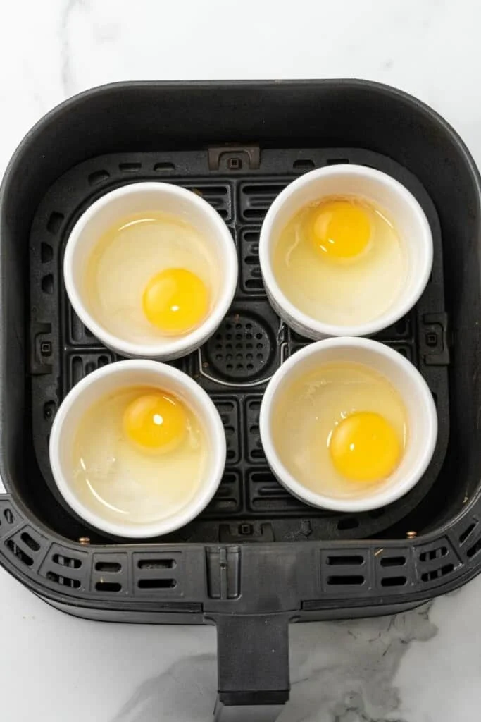 Ramekins filled with raw eggs, sitting in an air fryer.