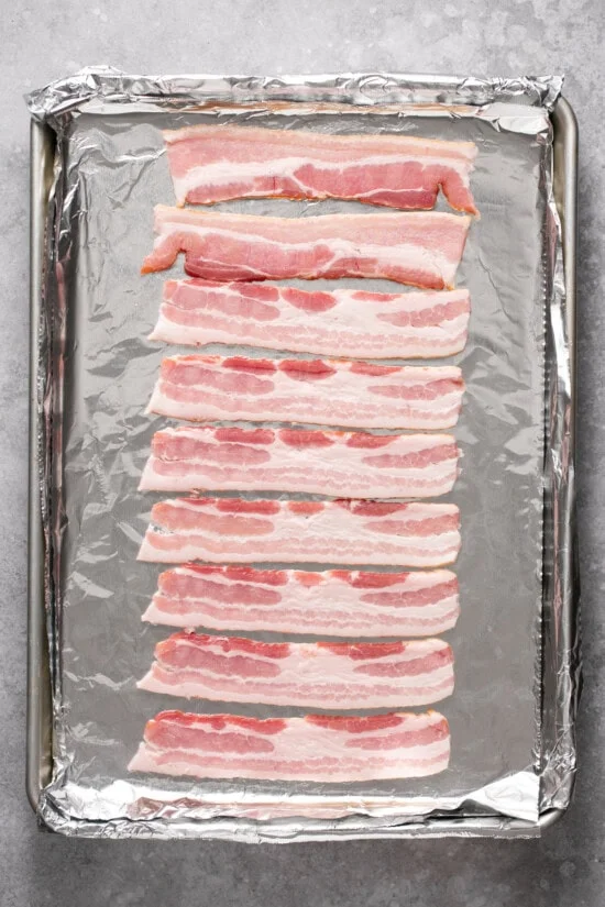 Raw bacon on a foil lined baking sheet.