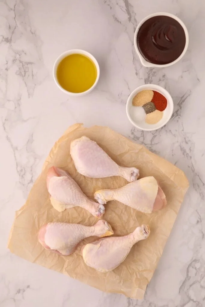 Raw chicken drumsticks on parchment paper.