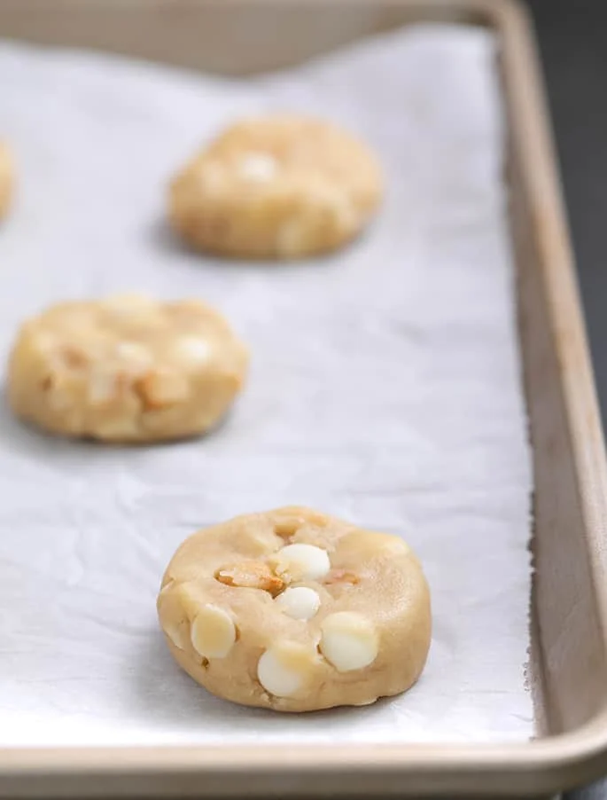 Raw cookie dough disks on white paper on a tray.
