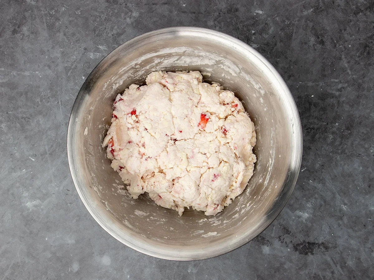 raw cream colored disk of raw biscuit dough with bright red bits of strawberries, still in mixing bowl