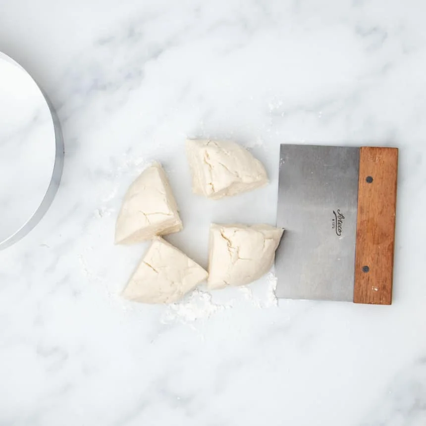 raw dough cut into 4 equal wedges with Ateco metal bench scraper with brown wood handle