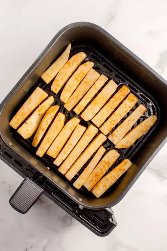 Raw french fries in an air fryer basket.
