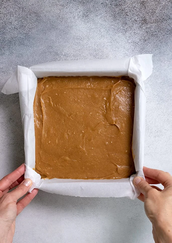 Raw gingerbread cake batter in square pan with hands holding sides of pan
