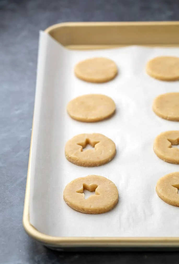 Raw linzer cookie rounds some with cutouts on white paper on tray