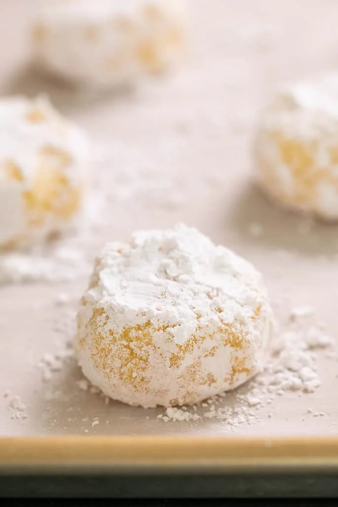 Raw mounds of yellow cookie dough with confectioners' sugar on white paper on gold metal tray