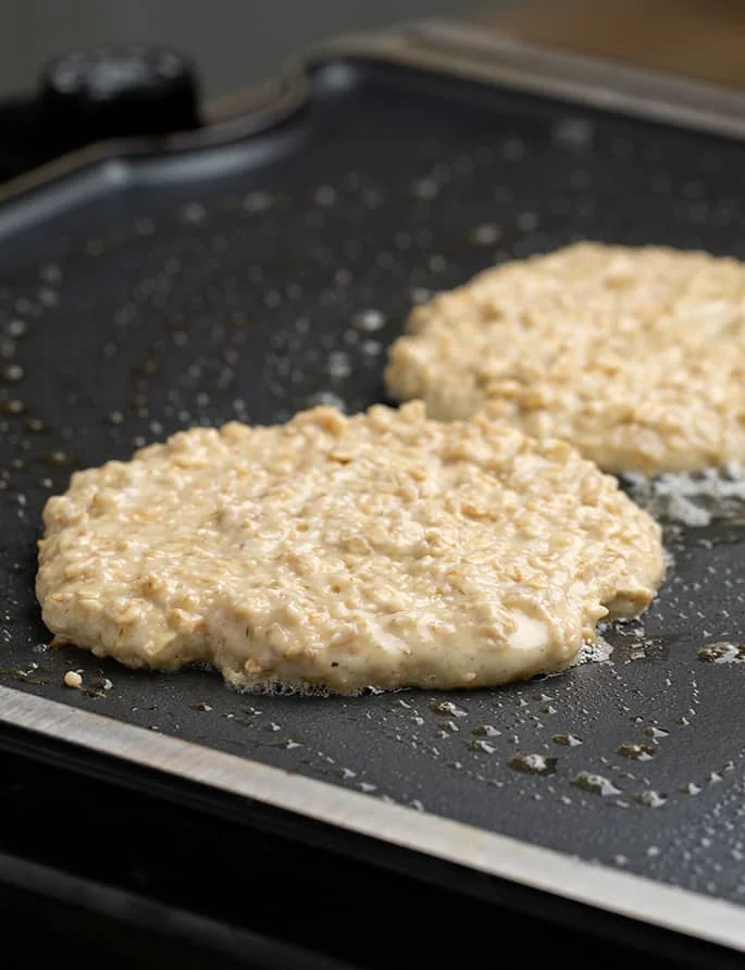 Raw oatmeal pancakes cooking on greased skillet