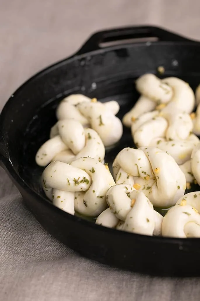 Raw, risen, shaped garlic knots with herbs and garlic in round cast iron skillet