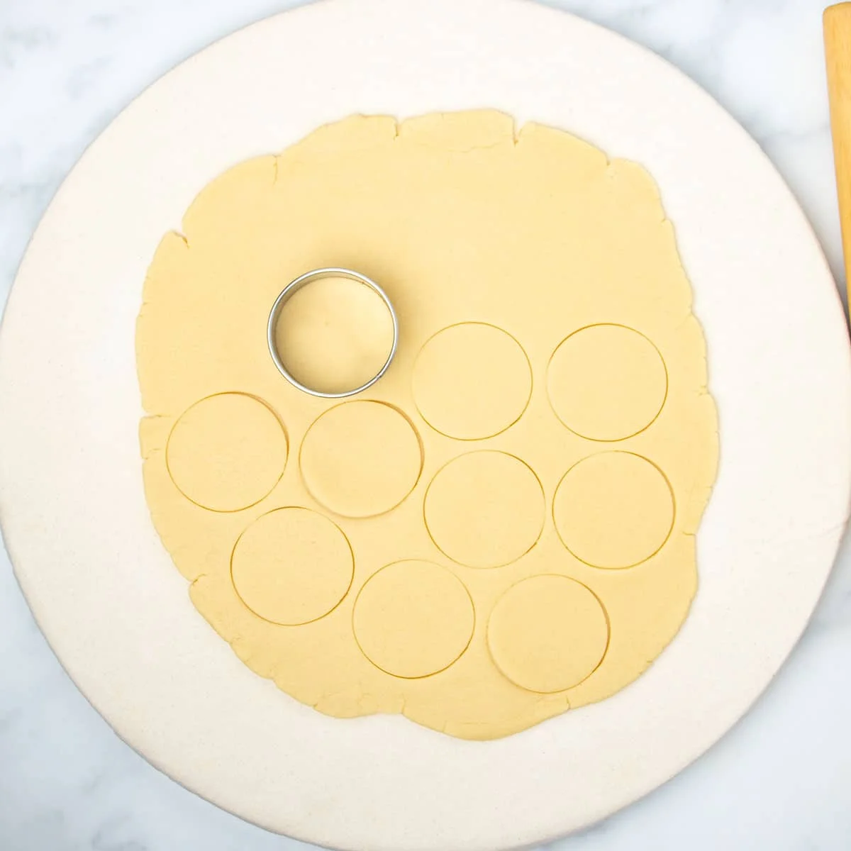 Raw round of rolled out dough with 9 rounds cut and round metal cookie cutter sitting on dough.