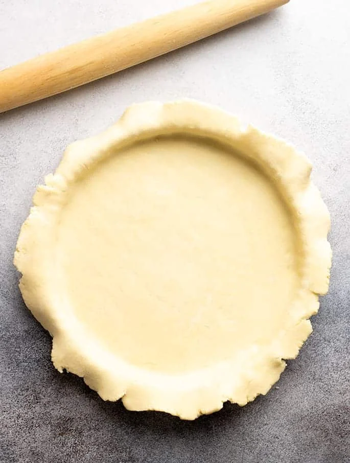 Raw savory tart crust draped over round tart pan with rolling pin on gray surface.