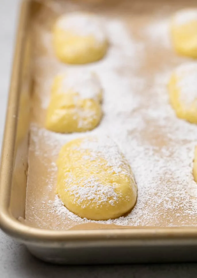 Raw shaped ladyfingers on brown paper on tray