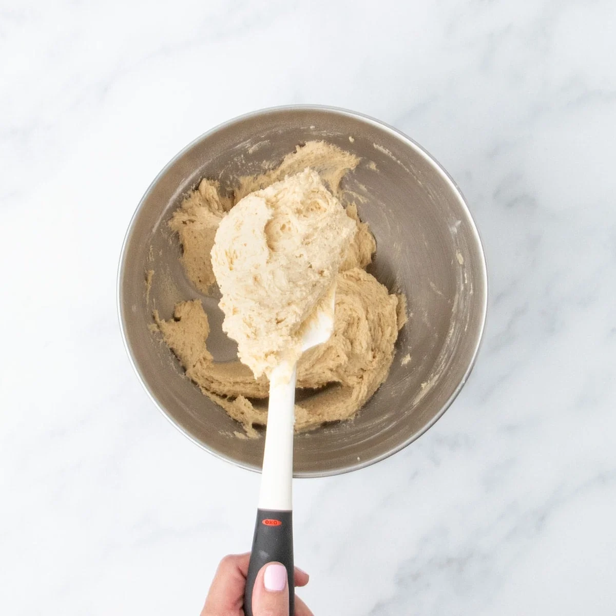 Raw snickerdoodle cookie dough partly on white spatula and partly in metal mixing bowl.