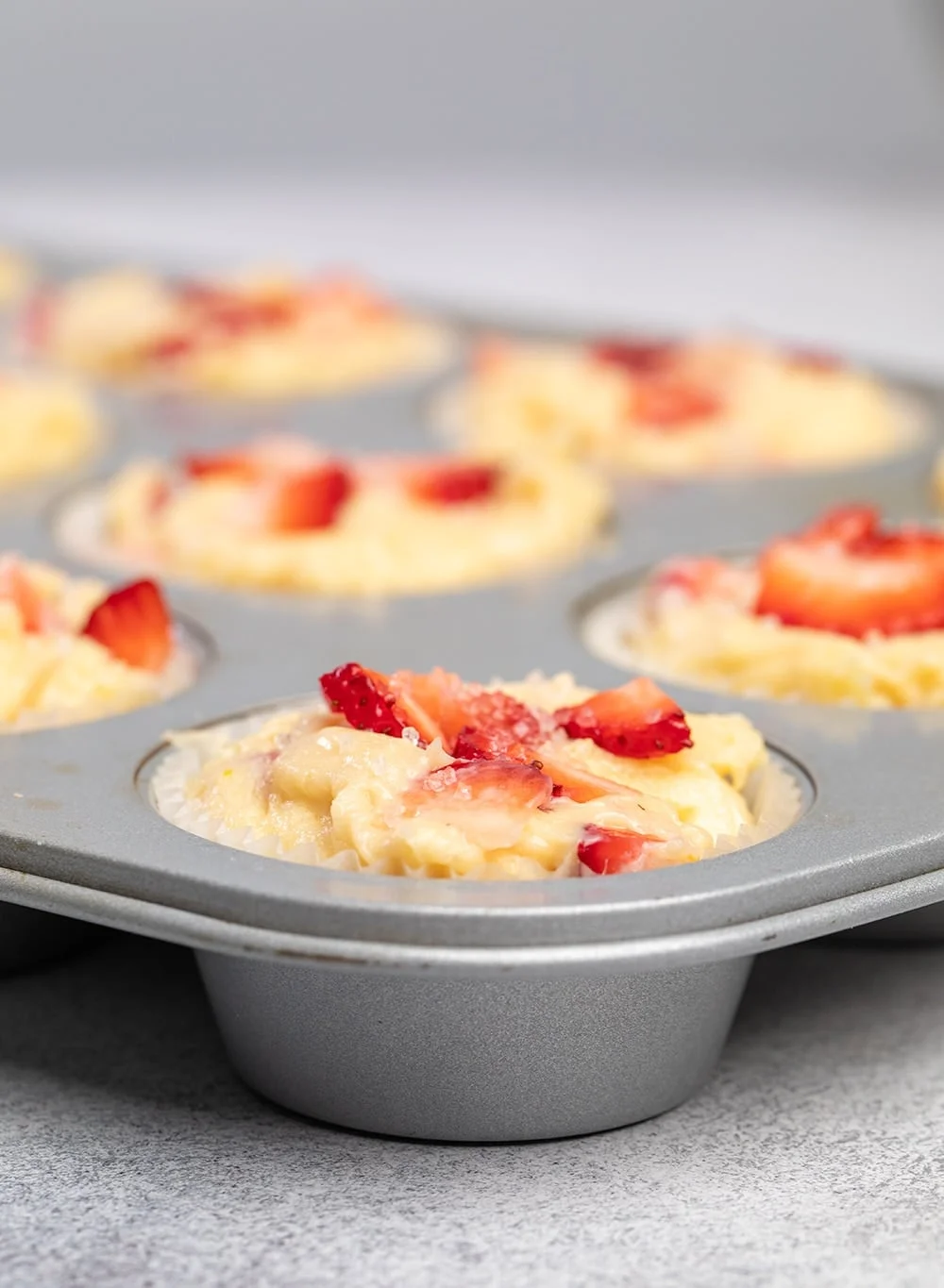 Raw strawberry muffins with chopped strawberries on top in muffin tin.