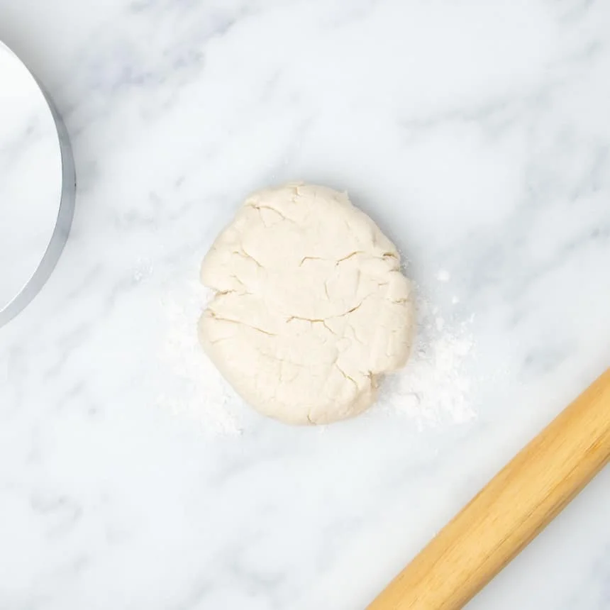 raw tortilla dough in disk on marble surface on top of scattered tapioca flour