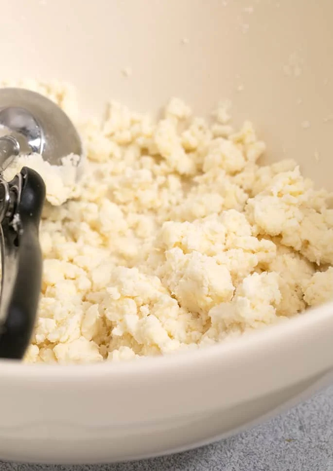 Raw unformed biscuit dough with ice cream scoop in large mixing bowl.