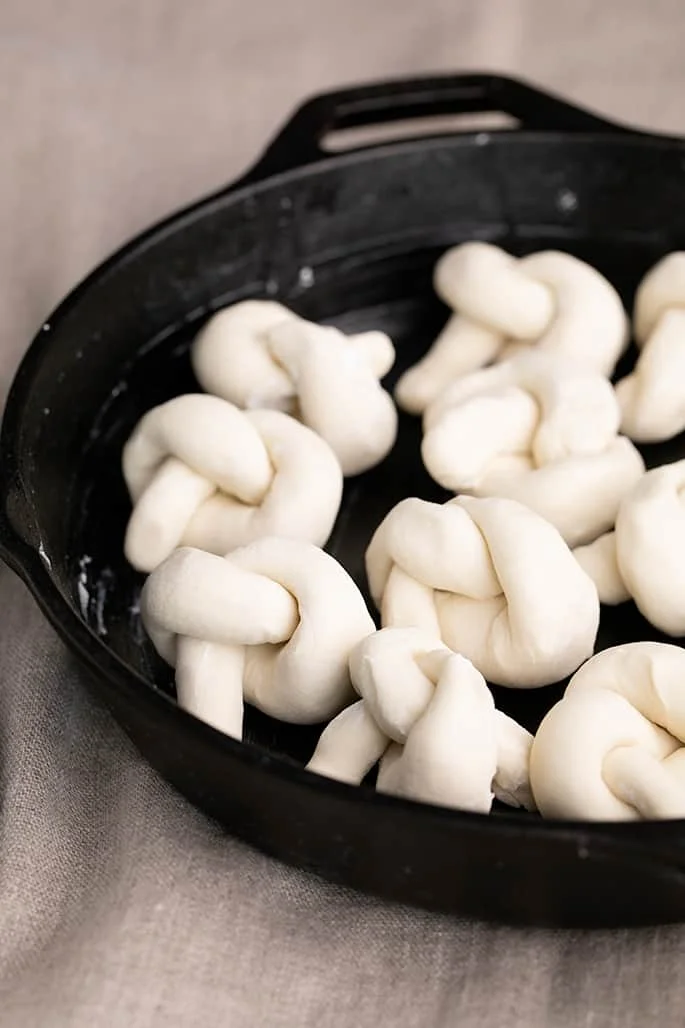 Raw, unrisen, shaped garlic knot dough pieces in round cast iron skillet
