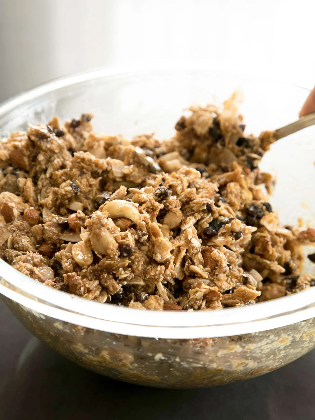 raw unshaped mixture for chewy granola bars in glass mixing bowl with mixing spoon