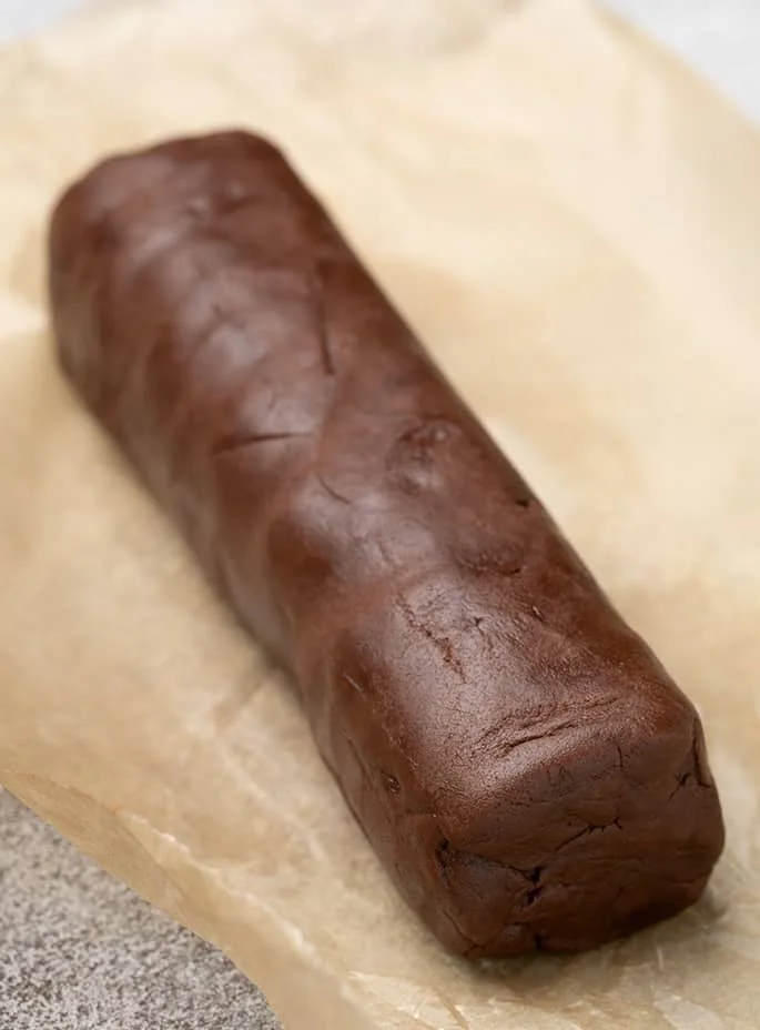 Rectangular log of brown cookie dough on light brown paper
