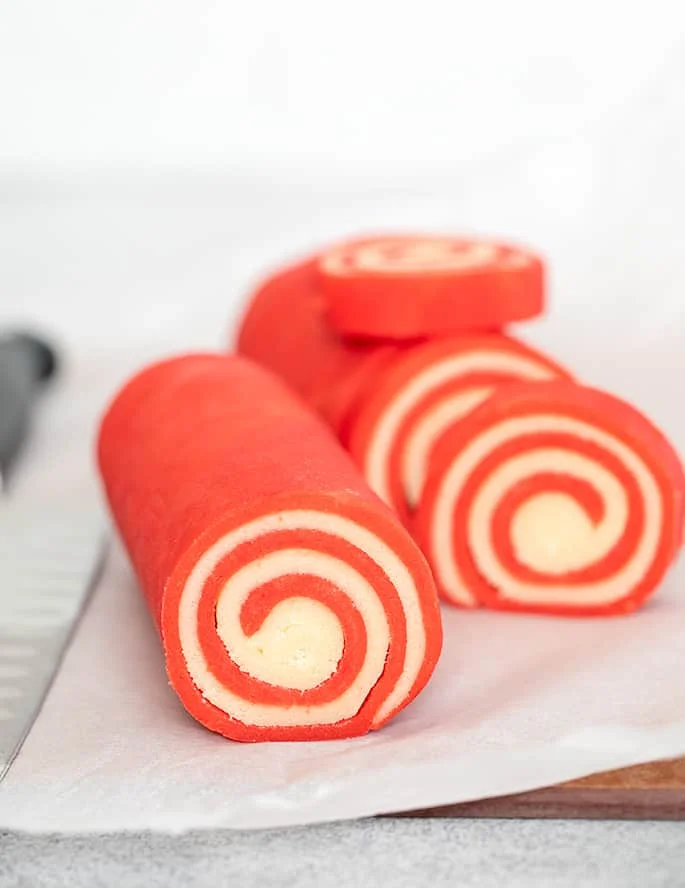 Red and white raw pinwheel cookie dough cut partially into slices.