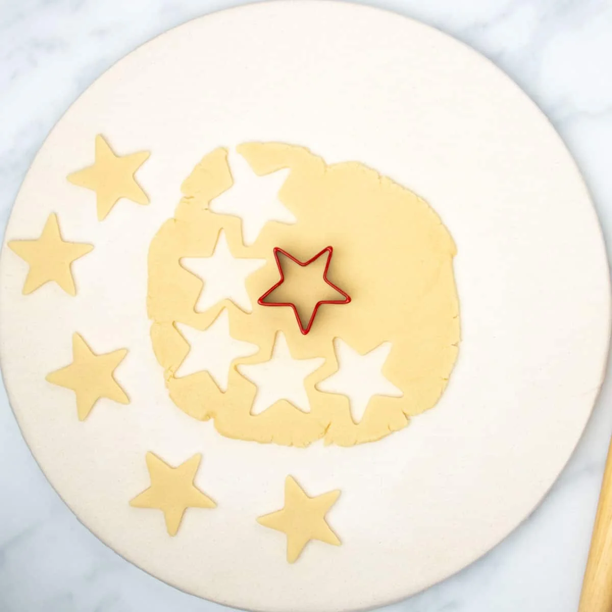 Rolled out raw dough with 5 star shapes cut out with red cookie cutter star.