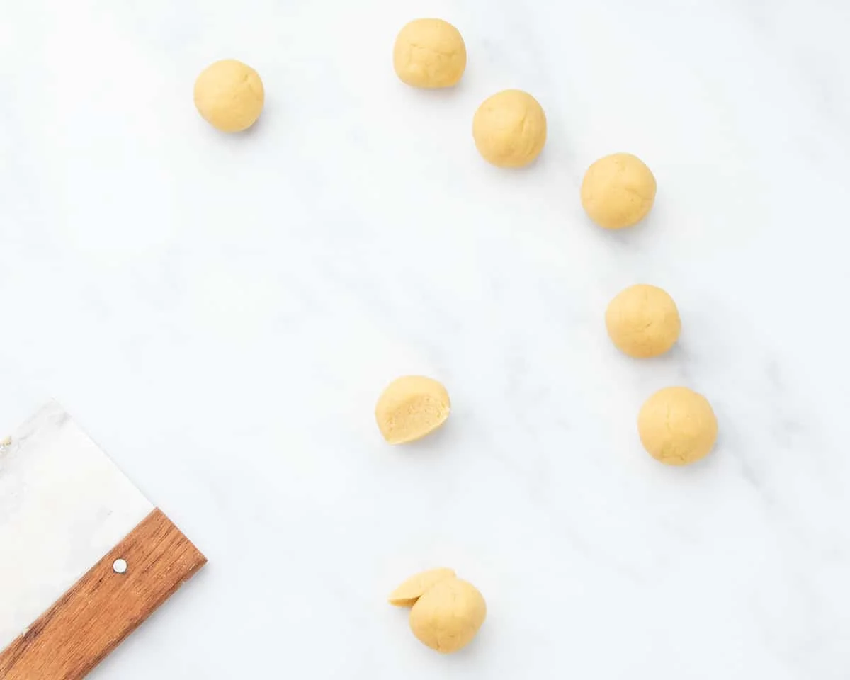 Round balls of raw dough waiting to be shaped with one ball reapportioned to make shaping easier.