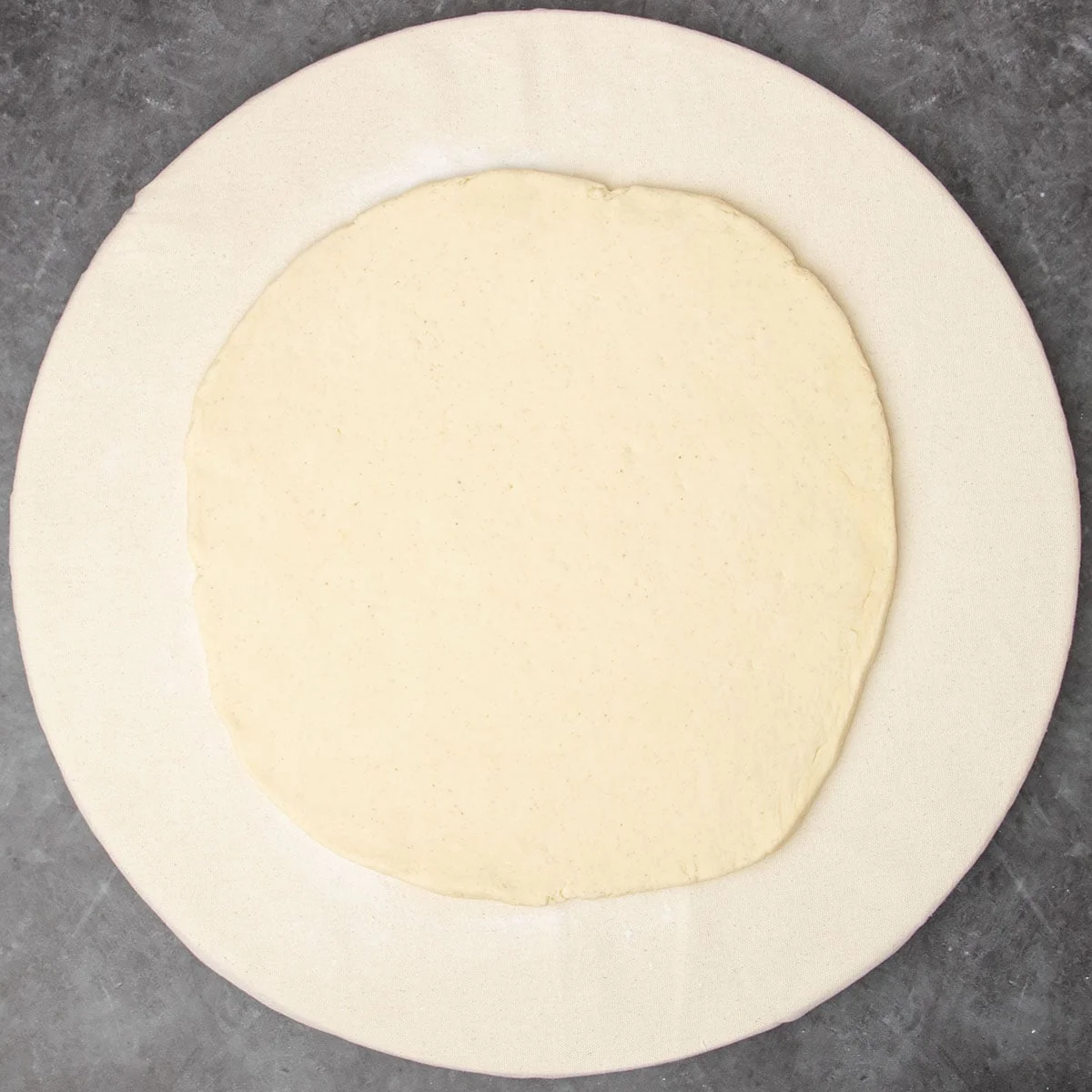 round board covered in light canvas cloth with 10-inch round dough rolled out on top