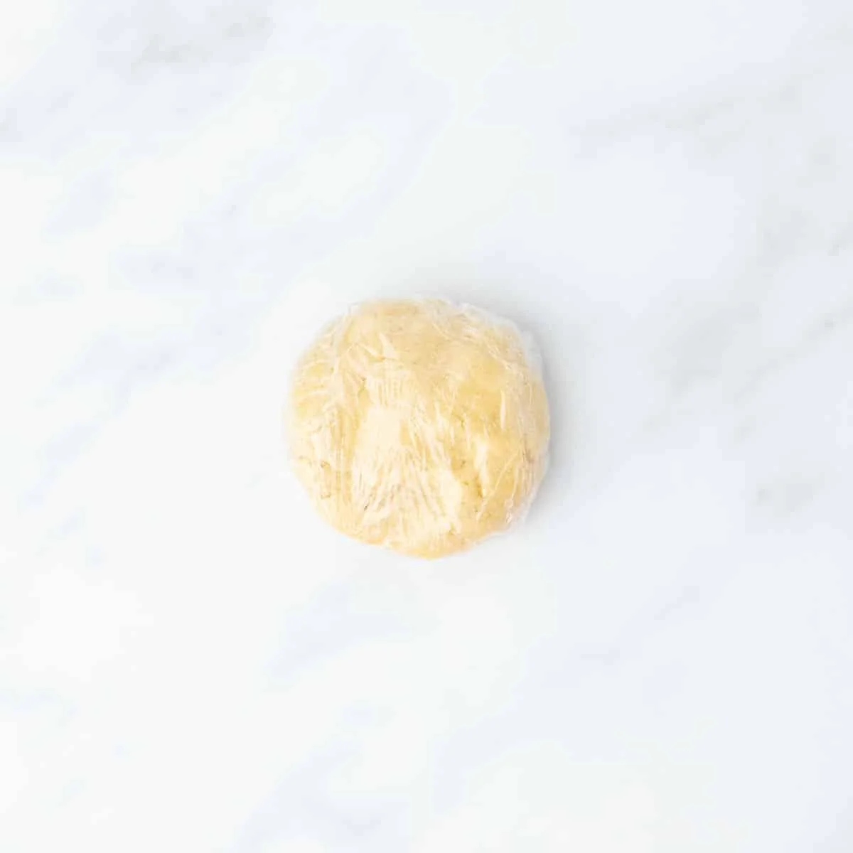 Round dough ball wrapped in plastic wrap, resting on a clean counter.