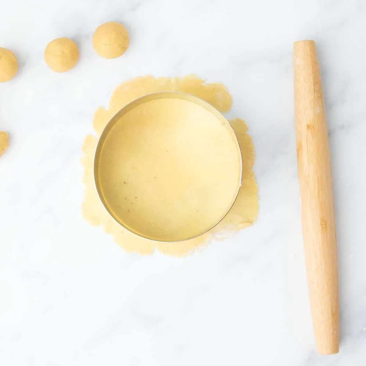 Round metal cutter placed over thinly rolled dough sheet.