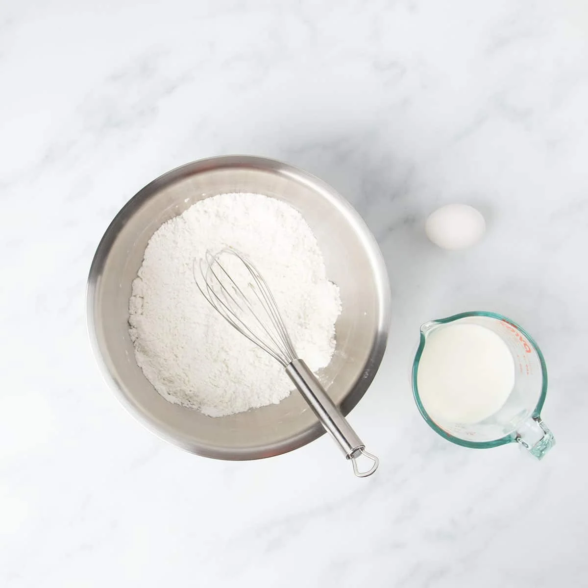 Round metal mixing bowl with white dry ingredients and wire whisk.