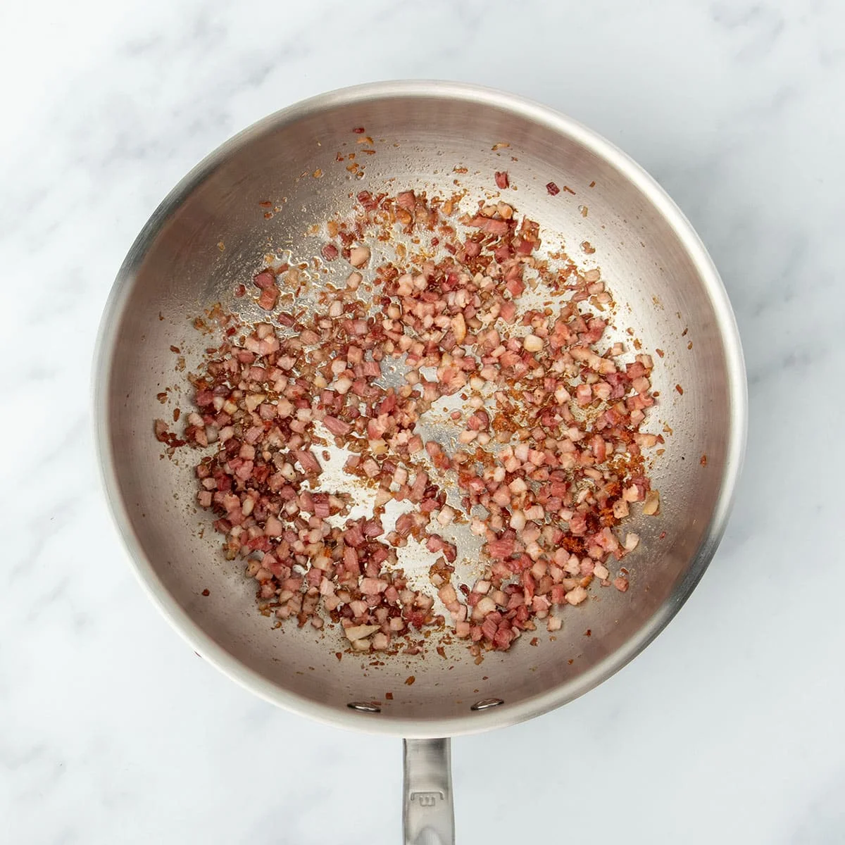 round metal saucier pan with handle with cooked cubed pink and brown pancetta