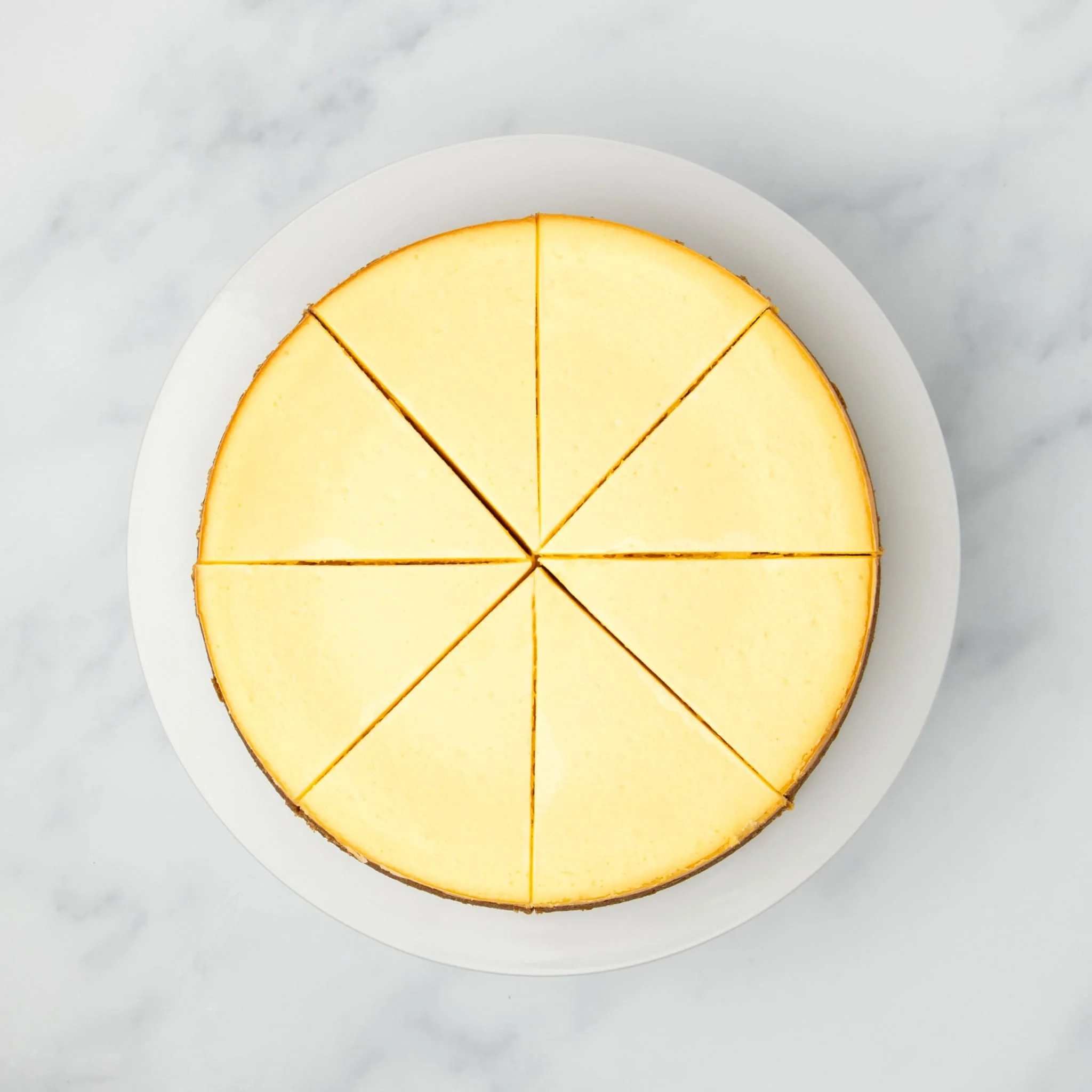 same baked cheesecake out of pan sliced into 8 triangles on a white plate