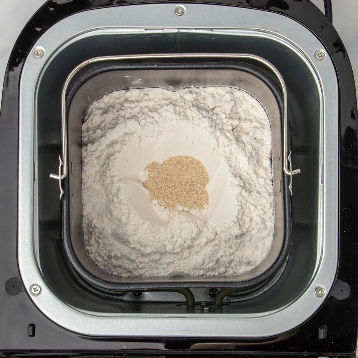 same baking pan with flour on top and instant yeast granules in small hole in center of flour in baking pan in bread machine