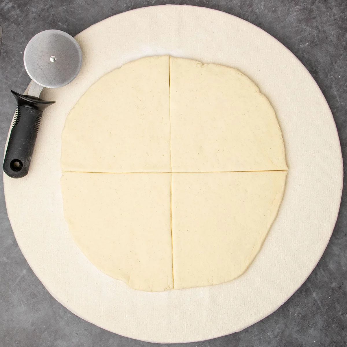 same board with round dough cut into 4 quarters with black-handled pizza wheel cutter