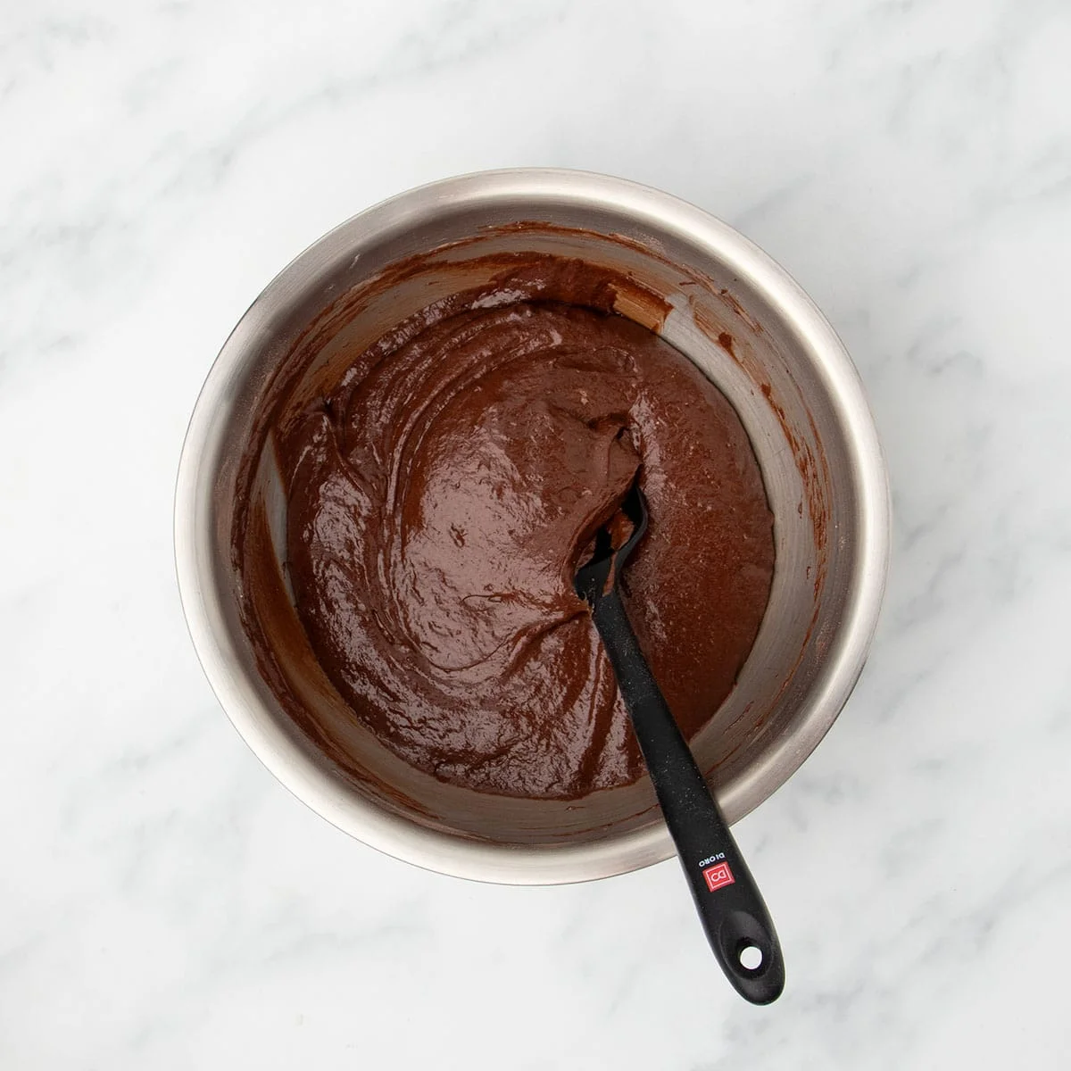 Same bowl with all ingredients mixed together with a black silicone spatula into a soft brown batter