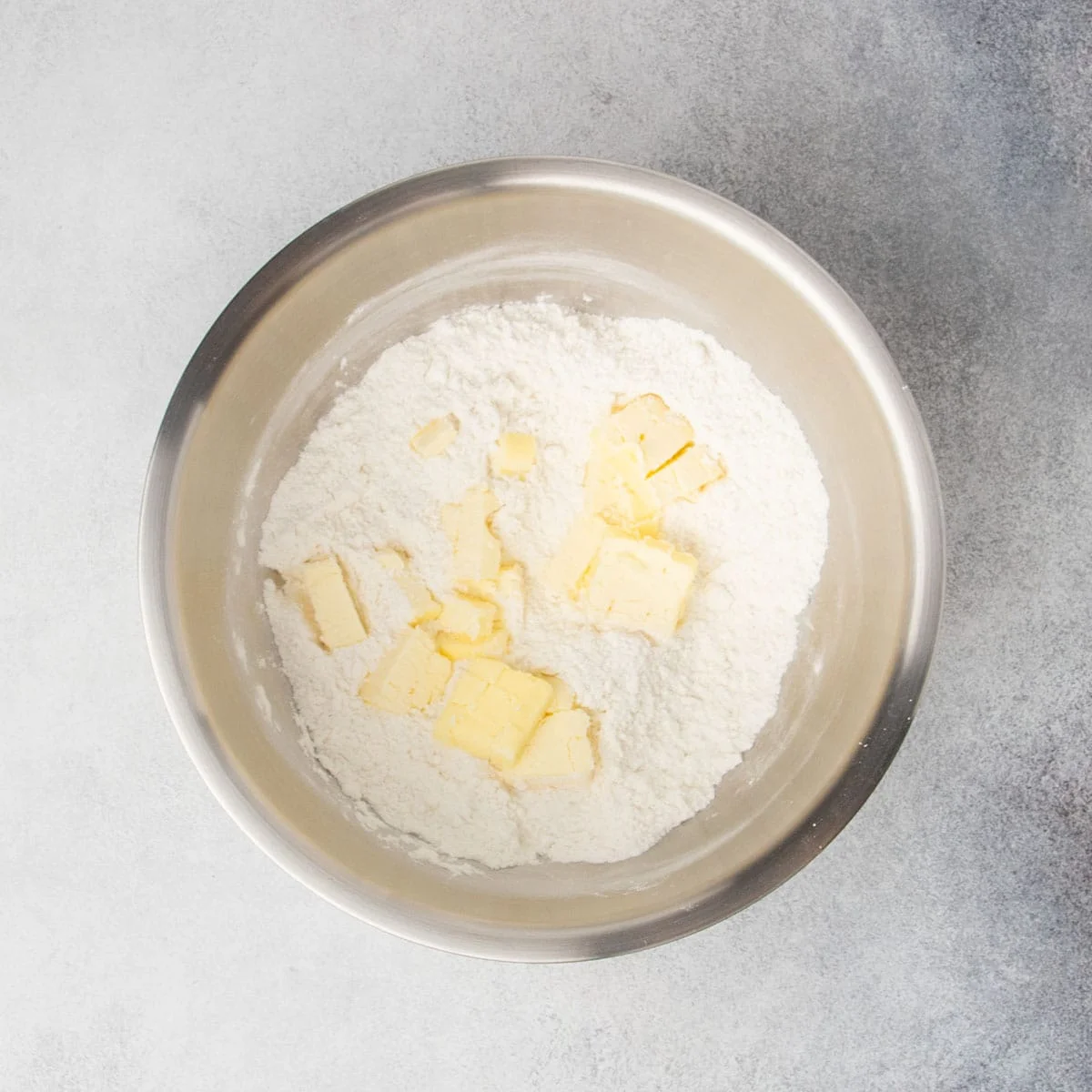 Same bowl with chopped yellow butter on top of flour mixture.