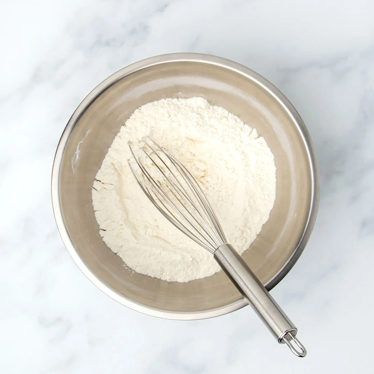 same bowl with pale white-tan powder whisked together with large metal wire whisk