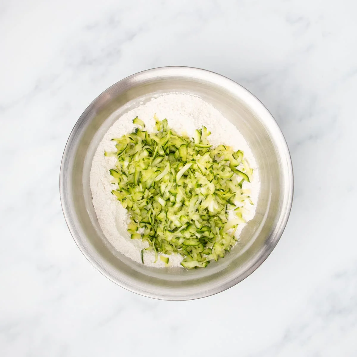 Same bowl with white flour mixture with green shredded zucchini on top.