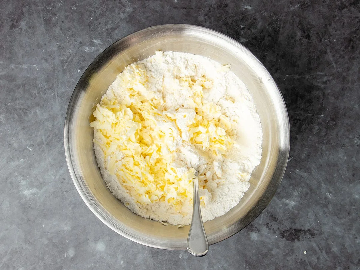 same bowl with yellow shreds of cold butter sitting on top with metal handle of mixing spoon