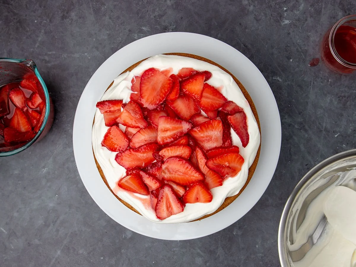 same cake with sliced strawberries on top of white whipped cream on cake