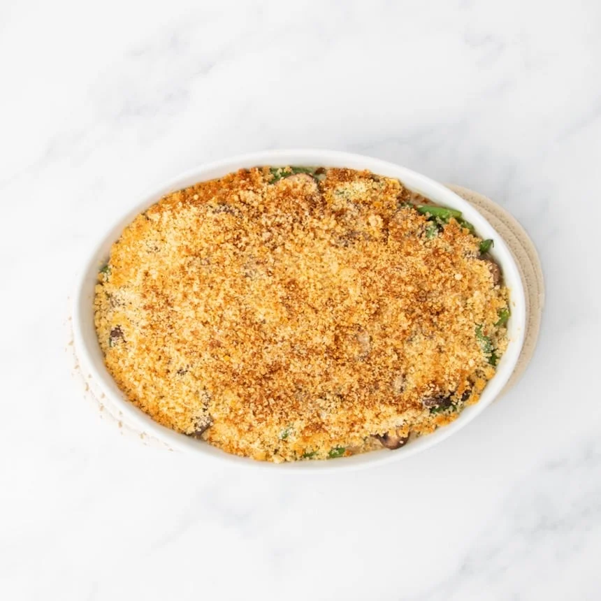 same casserole dish now with a golden brown topping after being baked in the oven, on cloth trivets to protect the marble countertop below